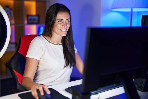 Jovem bela mulher hispânica streamer jogando videogame usando computador na sala de jogos