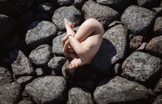 Jovem bela mulher nua posando em um quebra-mar de pedra. Morena nua curtindo a natureza