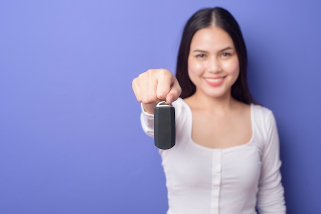 Jovem bela mulher sorridente está segurando a chave do carro isolado roxo