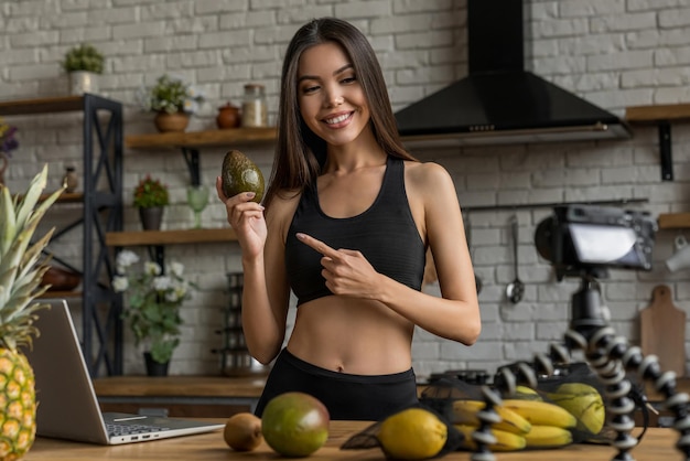 Jovem blogueira feminina com frutas gravando vídeo na cozinha