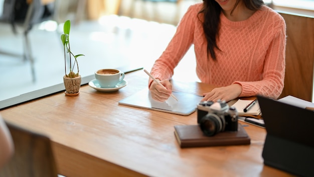 Jovem blogueira freelance com suéter confortável usando caneta stylus no computador tablet