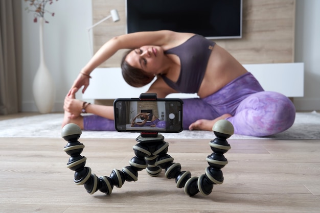 Jovem blogueira gravando vídeo de esportes em casa fazendo ioga na sala de estar