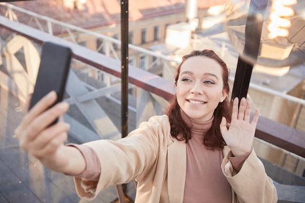 Jovem blogueira sorrindo para a câmera gravando vídeo em seu celular para seu blog