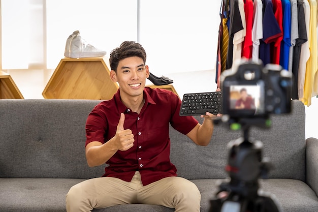 Jovem blogueiro comerciante online masculino asiático usando câmera para vídeo ao vivo para revisar e vender produtos com o polegar para cima Influenciador de mídia social e conceito de compras on-line