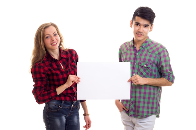 Jovem boa mulher com jovem bonito com cabelo escuro em camisas xadrez segurando cartaz branco