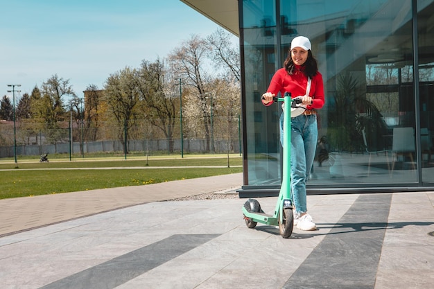 Foto jovem bonita anda de scooter elétrica para a lista de prédios de escritórios, transporte de milhas, estilo de vida urbano