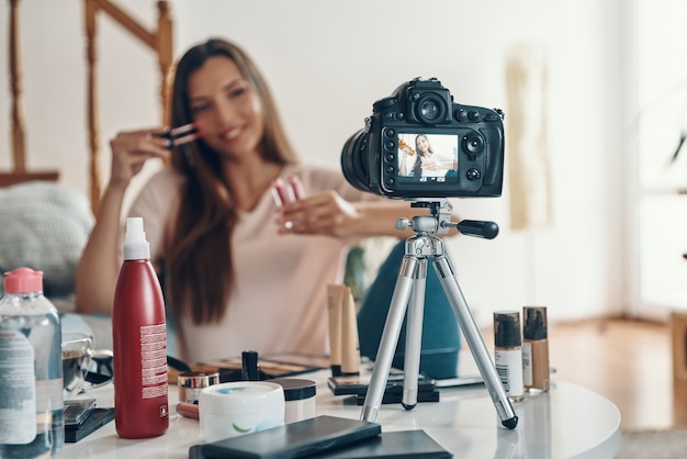 Jovem bonita aplicando brilho labial e sorrindo enquanto faz um vídeo nas redes sociais