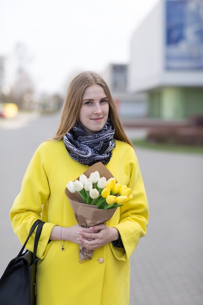 Jovem bonita com cabelos longos em um casaco amarelo e um buquê de flores nas mãos dela