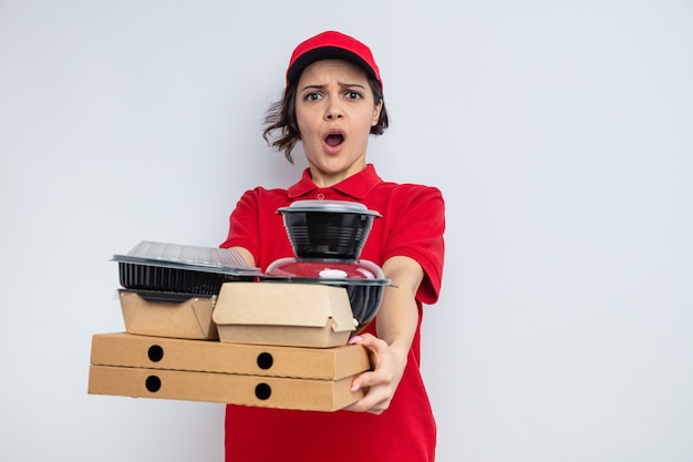 Jovem bonita entregadora ansiosa segurando recipientes de comida e embalagens em caixas de pizza