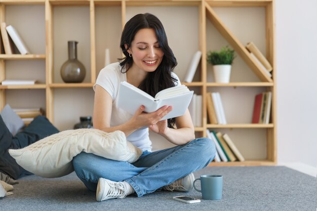 Jovem bonita lendo um livro enquanto está sentado em casa no fim de semana.