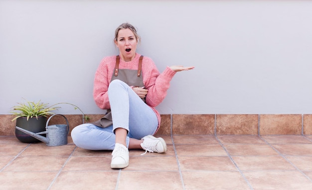 Jovem bonita loira jardineira sentada no chão com um espaço de cópia ao lado