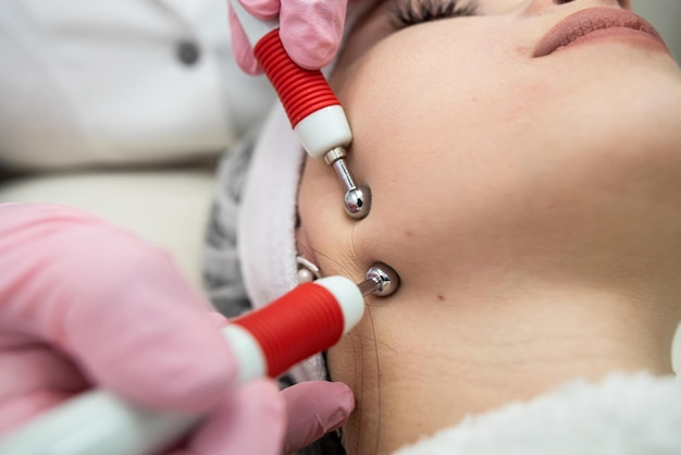 Foto jovem bonita recebendo tratamento facial elétrico estimulante de terapeuta na clínica de spa