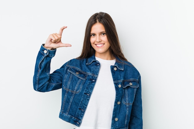 Jovem bonita segurando algo pouco com o dedo indicador, sorrindo e confiante.