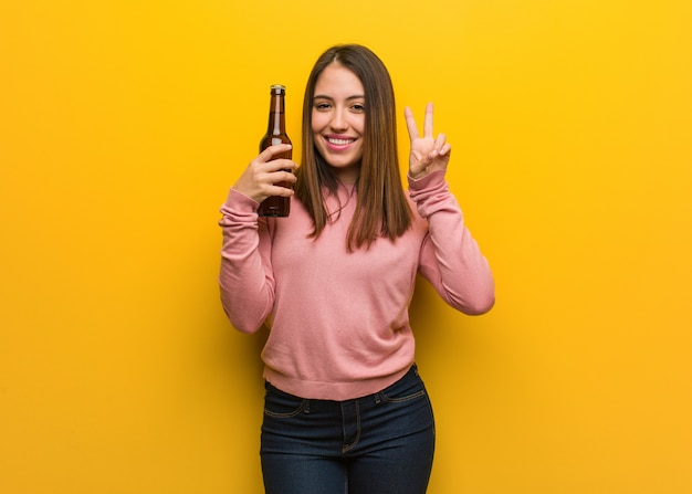 Jovem bonita, segurando uma cerveja, mostrando o número dois