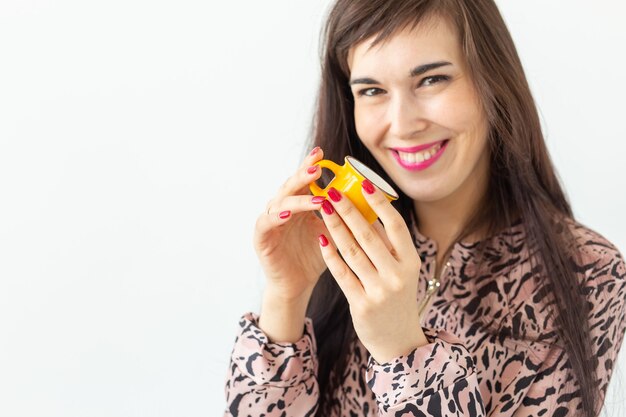 Foto jovem bonita segurando uma pequena caneca amarela de brinquedo nas mãos, posando em uma superfície branca com uma cópia