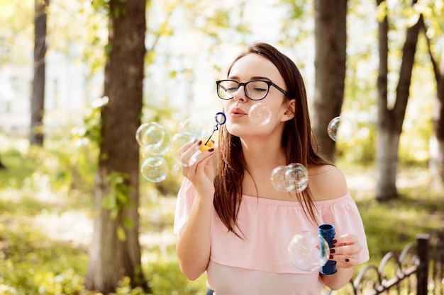 Jovem bonita soprando bolhas de sabão no parque em um dia ensolarado de verão
