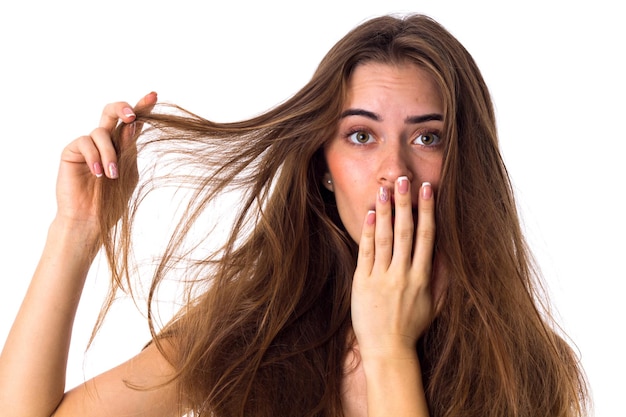 Foto jovem bonita tocando seu longo cabelo castanho emaranhado fechando a boca com a mão no fundo branco no estúdio