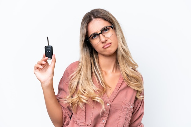 Jovem bonita uruguaia segurando as chaves do carro isoladas no fundo branco com expressão triste