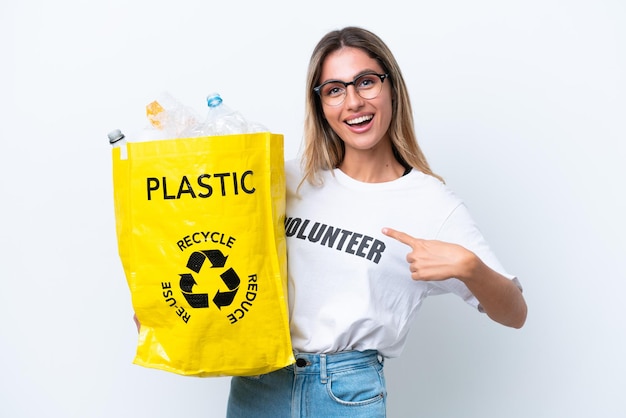 Jovem bonita uruguaia segurando um saco cheio de garrafas plásticas para reciclar isoladas no fundo branco com expressão facial de surpresa