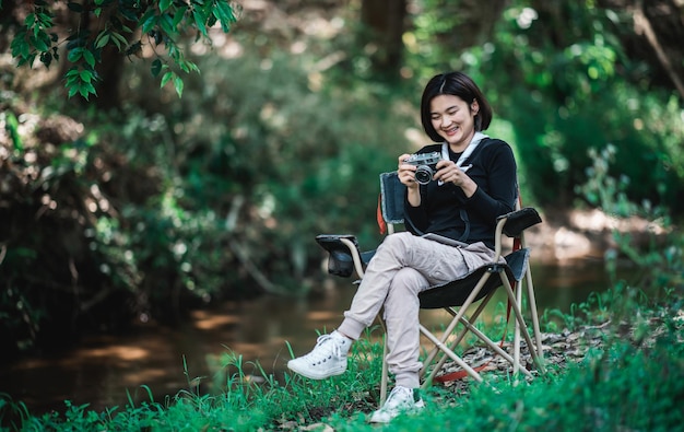 Jovem bonita usa câmera digital tirando uma foto linda natureza enquanto acampa na floresta com espaço de cópia de felicidade