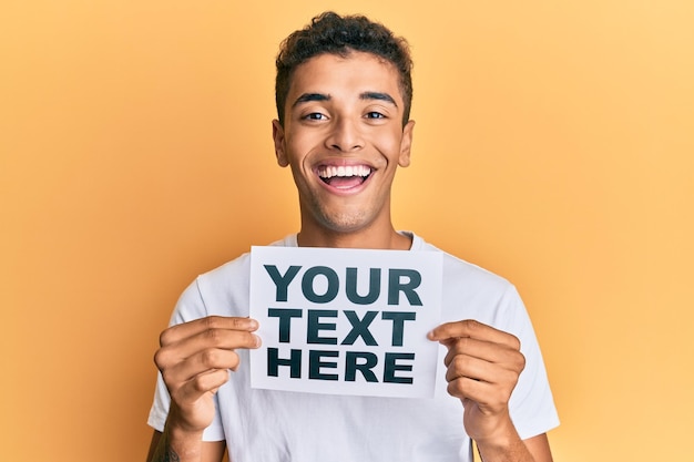 Jovem bonito afro-americano segurando seu texto aqui banner sorrindo e rindo muito alto porque uma piada louca e engraçada.