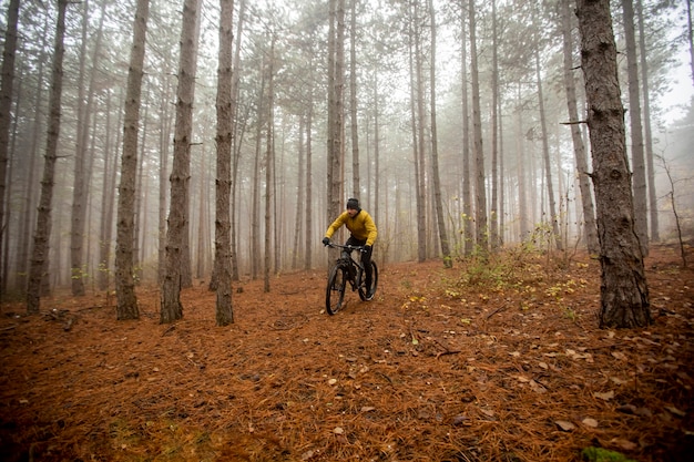 Jovem bonito andando de bicicleta pela floresta de outono