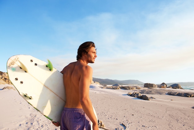 Foto jovem bonito andando na praia com prancha de surf