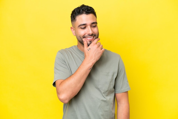 Jovem bonito árabe isolado em fundo amarelo, olhando para o lado e sorrindo