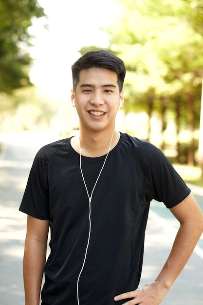 Jovem bonito asiático correndo ao ar livre ouvindo música no parque