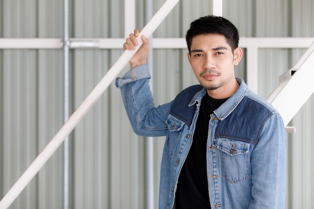 Jovem bonito asiático na jaqueta jeans em pé e pose em um gesto de estilo moderno. Conceito de retrato urbano na moda.