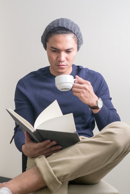 Jovem bonito asiático sentado lendo um livro e bebendo café