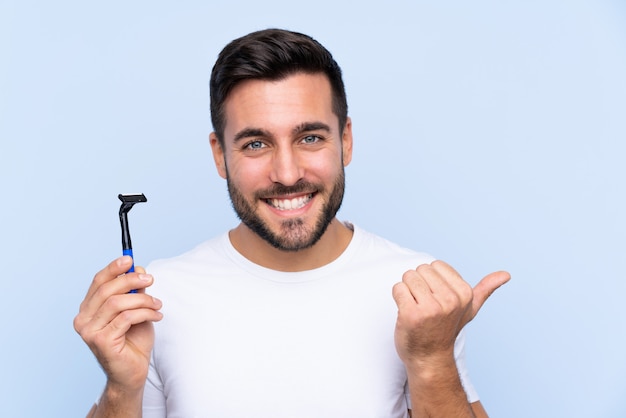 Jovem bonito barbear a barba sobre parede isolada, apontando para o lado para apresentar um produto