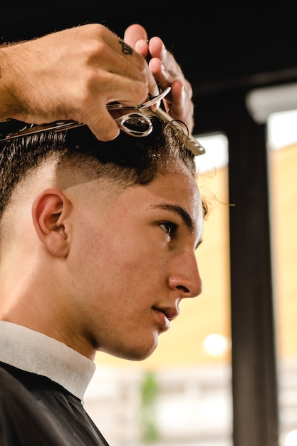 Jovem bonito barbeiro fazendo corte de cabelo de adolescente homem na barbearia