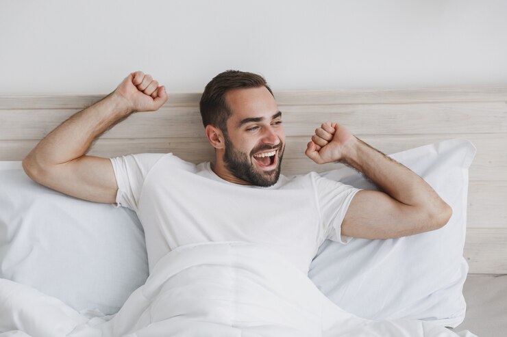 Foto jovem bonito barbudo calmo deitado na cama com lençol branco e cobertor no quarto em casa