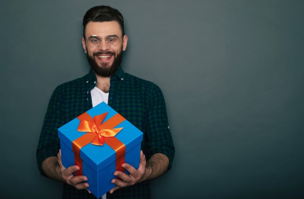 Foto jovem bonito barbudo feliz no casual wear de bom humor com uma grande caixa de presente nas mãos, se divertindo e posando