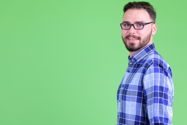 jovem bonito barbudo hippie homem com óculos contra chroma key com parede verde