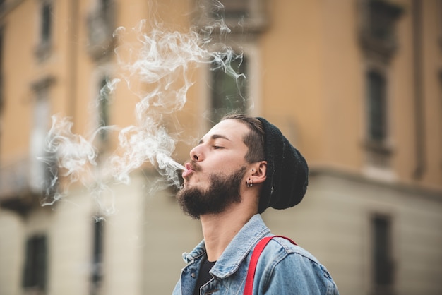 Foto jovem bonito barbudo hipster homem fumando cigarro