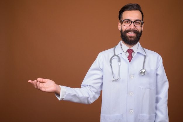 Jovem bonito barbudo médico persa na parede marrom