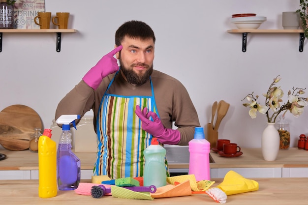 Jovem bonito barbudo na cozinha, mostra toda a sua equipe de limpeza - detergentes, escovas, sprays. Ele acha que está pronto para uma limpeza real