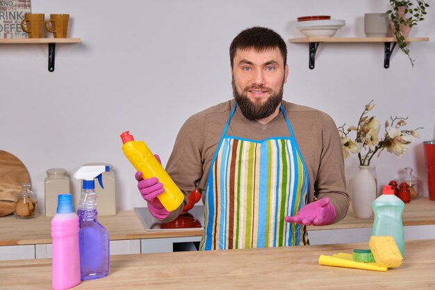 Jovem bonito barbudo na cozinha se limpa usando spray de detergente e escova