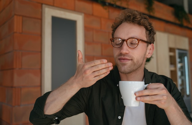 Jovem bonito bebendo café cheirando aroma de bebida sentado no café Conceito de pausa para café