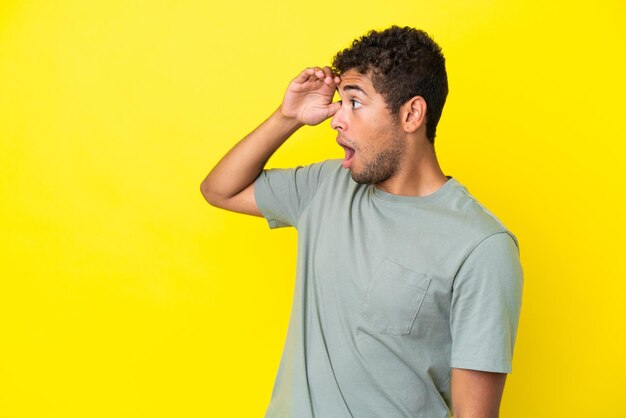 Jovem bonito brasileiro isolado em um fundo amarelo com expressão de surpresa ao olhar de lado