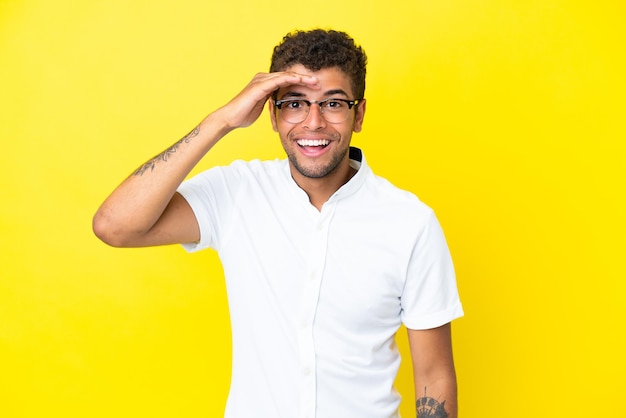 Jovem bonito brasileiro isolado em um fundo amarelo olhando para longe com a mão para olhar algo