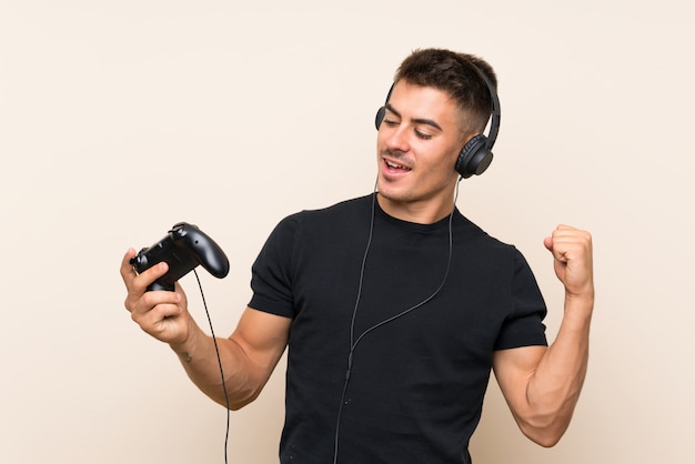 Jovem bonito brincando com um controlador de videogame sobre parede comemorando uma vitória