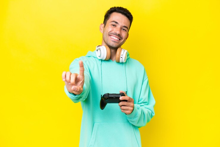 Foto jovem bonito brincando com um controlador de videogame sobre parede isolada mostrando e levantando um dedo