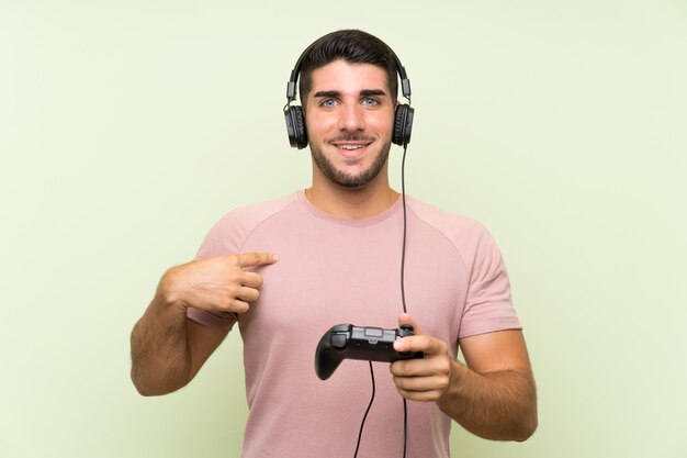 Jovem bonito brincando com um controlador de videogame sobre parede verde isolada com expressão facial de surpresa