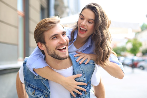 Jovem bonito carregando uma mulher atraente nos ombros enquanto passam algum tempo juntos ao ar livre.