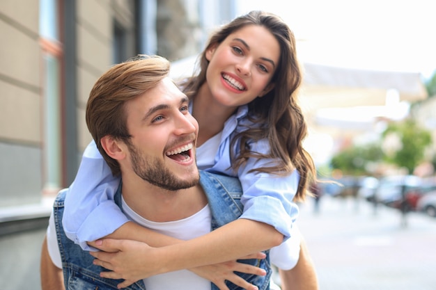 Jovem bonito carregando uma mulher atraente nos ombros enquanto passam algum tempo juntos ao ar livre.