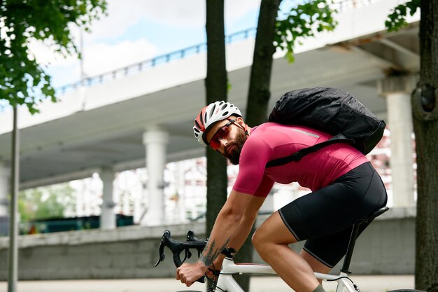 Jovem bonito caucasiano no capacete protetor sai para passeio de bicicleta pelas ruas da cidade em fundo desfocado Ciclista masculino passeio de bicicleta ao ar livre em urbano