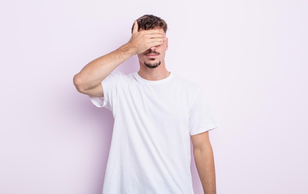 Jovem bonito cobrindo os olhos com uma mão, sentindo-se assustado ou ansioso, imaginando ou esperando cegamente por uma surpresa